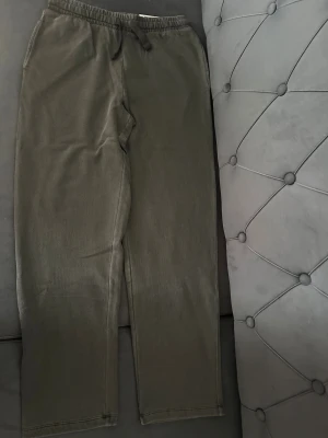 Mörkgrå relaxed mjukisbyxor C 158/164 - Snygga mörkgrå mjukisbyxor från C i relaxed fit med elastisk midja och snörning. Tillverkade i bomull med pigment dye för cool tvättad look. Perfekta för chill dagar och sköna att bära hela tiden.