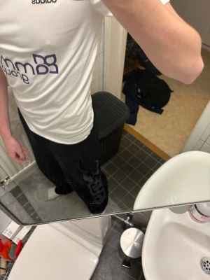 Svarta mjukisbyxor från Gasp - Svarta mjukisbyxor från Gasp med stort grått tryck längs ena benet. Byxorna har snörning i midjan och är tillverkade i mjukt bomullsmaterial. Passformen är loose och de har raka ben. Perfekta för chill eller träning.