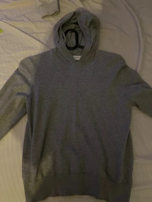 Strl M/150 - En enkel och stilren grå hoodie från Grunt i storlek M. Tröjan har huva och långa ärmar, perfekt för chill dagar. Materialet känns mjukt och skönt mot huden, och den har en klassisk passform med ribbade muddar vid ärmslut och nederkant.