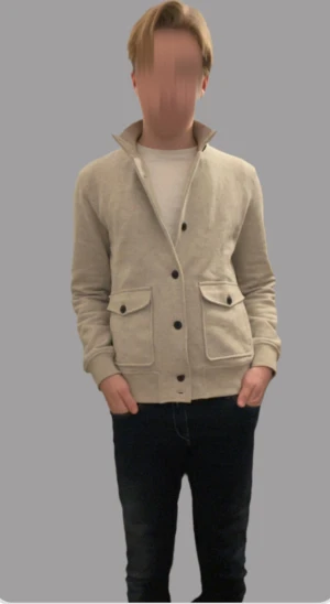 Beige cardigan jacka från Morris XS - Snygg beige cardigan jacka från Morris i bomull. Jackan har hög krage, stora fickor med lock och knappar framtill. Perfekt för dig som gillar stilren och enkel design med en modern touch.