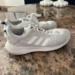 Vita Adidas Climacool sneakers - Säljer ett par fräscha vita Adidas Climacool sneakers med klassiska tre ränder på sidan. Skorna har mesh-överdel för bra andningsförmåga och en mjuk, bekväm sula. Perfekta för dig som gillar stilrena och sportiga skor.