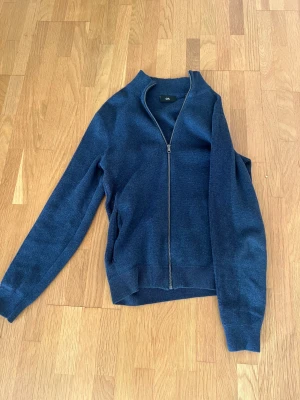 Marinblå stickad kofta från C&A - Snygg marinblå stickad kofta från C&A i storlek S. Koftan har hel dragkedja framtill, ribbade muddar och en enkel, stilren design. Perfekt för dig som gillar klassiska plagg med modern touch. Passar till många olika outfits och är superbekväm.