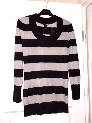 Randig långärmad tröja från H&M - Snygg långärmad tröja från H&M med breda svarta och grå ränder. Tröjan har rundad halsringning och är stickad med ett lätt glittrigt material som ger extra vibe. 
