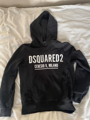 Svart hoodie från Dsquared2 - Svart hoodie från Dsquared2 med stor vit logotyp och texten 'Ceresio 9, Milano' på bröstet. Klassisk huva och ribbade muddar vid ärmslut och nederkant. Perfekt för dig som gillar streetwear och snygga märkesplagg.