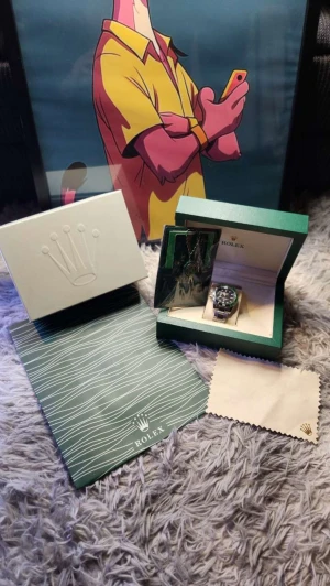  Submariner med grön bezel - Submariner med grön bezel och svart urtavla. Klockan har en rund form och är tillverkad i silverfärgat stål med klassisk länkarmband. Levereras med originalbox, certifikat och putsduk. Perfekt för dig som gillar ikonisk design och vill ha något riktigt stilrent på handleden.