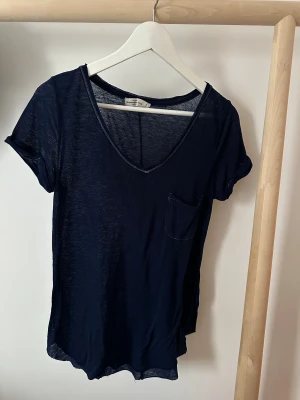 Mörkblå t-shirt från Abercrombie & Fitch - Snygg mörkblå t-shirt från Abercrombie & Fitch i tunn bomull. Modellen har v-ringad hals, korta ärmar med uppvik och en liten bröstficka. 
