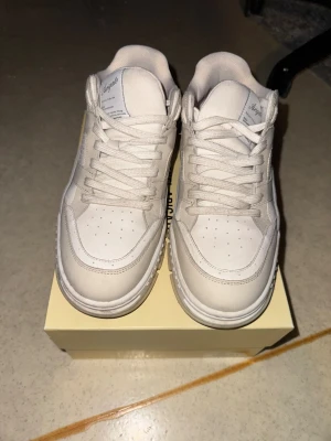 Vita sneakers från Axel Arigato - Snygga vita sneakers från Axel Arigato med klassisk siluett och låg profil. Skorna har snörning, perforerade detaljer på tån och är tillverkade i skinn och textil. Perfekta för dig som gillar stilrena och cleana sneakers med diskret branding på sidan. Box dustbag medföljer osäker om kvittot finns på mail