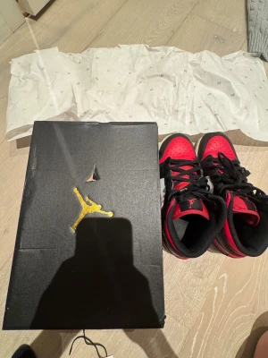 Nike Air Jordan 1 High röd/svart/vit - Nike Air Jordan 1 High sneakers i klassisk röd, svart och vit färgkombination. Skorna har snörning, rund tå och platt sula. Ikonisk Air Jordan-logga på sidan och Jumpman på tungan. Tillverkade i skinn med textilfoder, perfekt för dig som gillar streetstyle och sneakers med retro vibe.