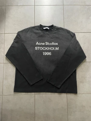 Svart långärmad tröja Acne Studios - Svart långärmad tröja från Acne Studios med tryck 'Acne Studios STOCKHOLM 1996' på bröstet. Tröjan har en klassisk rund hals och är tillverkad i mjuk bomull. Passformen är normal och stilen är enkel men stilren, perfekt för dig som gillar minimalistisk design.
