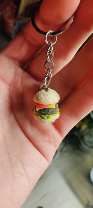 Nyckelring miniatyrhamburgare - Unik nyckelring med en miniatyrhamburgare som hänge. Hamburgaren har detaljer i beige, brun, grön, gul och röd och är fäst i en silverfärgad kedja med nyckelring. Perfekt accessoar för dig som gillar roliga och annorlunda smycken.