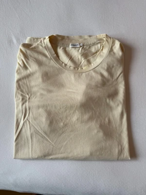 Beige t-shirt från Filippa K i bomull - En stilren beige/ljusgul t-shirt från Filippa K i mjuk bomull. Klassisk rund halsringning och korta ärmar. Perfekt basic-plagg med clean look och skön passform. Enkel att matcha med allt i garderoben.