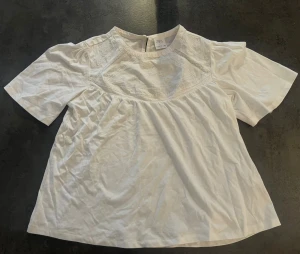 Vit blus från Zara med broderi - Säljer en söt vit blus från Zara med korta ärmar och broderade detaljer upptill. Blusen har en rund halsringning och är gjord i mjuk bomull. Perfekt för dig som gillar en clean och fräsch look med lite extra detaljer. Blusen är till för 13-14 (164) men skulle säga den sitter som storlek S.
