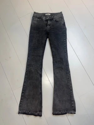 Svarta bootcut jeans med rå kant - Snygga svarta bootcut jeans med rå, fransad kant längst ner. Jeansen har klassisk femficksdesign och en mörk tvätt som ger en cool vibe. Materialet är stretchigt denim för skön passform och midjan är normal. Perfekta för dig som gillar en trendig siluett.