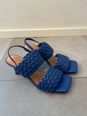 Blå flätade sandaler med klack - Snygga blå klackar från Sofie Schnoor med flätade remmar och fyrkantig tå. De har en låg klack och öppen häl.