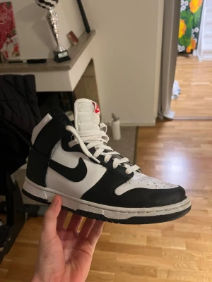 Nike Dunk  svart/vit sneakers - Nike Dunk  sneakers i svart och vitt med klassisk Swoosh på sidan. Skorna har snörning, rund tå och platt sula. Tillverkade i skinn med textilfoder och högt skaft för extra support. Perfekt för dig som gillar retrostil och streetwear.