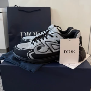 Dior B30 sneakers svart och grå - Säljer ett par Dior B30 sneakers i svart och grå med coola kontraster och CD-logga på hälen. Skorna har mesh och syntetpaneler, snörning och en chunky platt sula. Perfekt för dig som gillar exklusiv streetstyle och vill sticka ut med designer på fötterna. Använd cirka 2 gånger! 