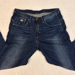 G-Star RAW mörkblå jeans - Snygga mörkblå jeans från G-Star RAW med klassisk look och coola slitningar. Jeansen har slim fit , kontrastsömmar och detaljerade fickor med logopatch framtill. Perfekt för dig som gillar grisch stileb och vill ha en avslappnad look.