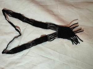 Svart pärlhalsband med fransar - Unikt svart halsband gjort av små och avlånga pärlor, med coola fransdetaljer i ena änden. Halsbandet har ett flätat utseende och är cirka 35 cm långt. Perfekt för dig som gillar statement-smycken och vill sticka ut med något annorlunda.