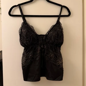 Spetslinnetopp - Svart satin topp med guldigt mönster. Köpte den av någon annan som sa att den var storlek xs, men jag skulle uppskatta den till s. Finns alltså ingen lapp inuti.