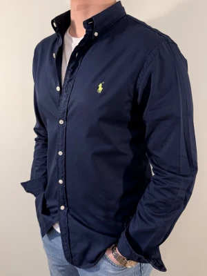 Mörkblå Ralph Lauren skjorta - En snygg polo skjorta som passar till alla tillställningar! Väldigt bra allround för festliga högtider som nyår eller vanliga sommarkvällar. Skjortan har inga deffeker och är i slim fit.  Storlek👔: M Nypris💰: ca 1399 kr