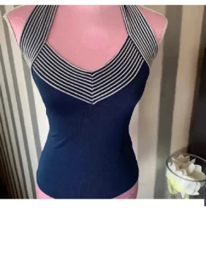 Marinblå randig halterneck linnetopp - Snygg marinblå linnetopp med vita ränder upptill och halterneck-modell. Toppen är figurnära och har en sportig känsla med sitt randiga mönster runt halsen. Perfekt till sommaren och enkel att matcha med jeans eller kjol.