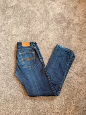 Nudie Slim Jim 30x32 - Nudie jeans i storlek 30x32! Modellen heter Slim Jim, sitter som slim/straight och är lite flared. Riktigt snygga jeans som fått bra fades. | Midja: 42cm | Lår: 25,5cm | Ytterbenslängd: ca 102cm | Benöppning: 20cm | Nypris: 1400kr, mitt pris: 749kr. Skriv vid minsta fundering!
