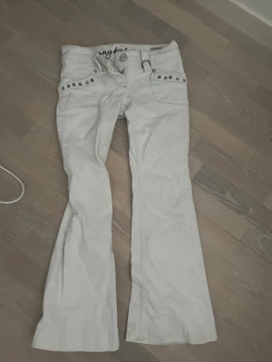 Vita bootcut jeans med nitar - Säljer ett par vita bootcut jeans från Jennyfer med coola nitar på fickorna och broderad detalj bak. Jeansen har låg midja och är tillverkade i bomull. Snygg passform och jätte fina detaljer som gör dem unika.