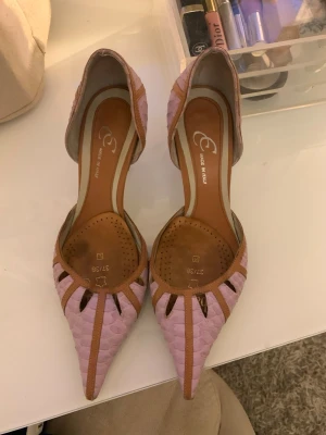 Lila/rosa klackar  - Säljer ett par unika pumps i lila/rosa med spetsig tå och snygga utskärningar. Skorna är tillverkade i skinn  med ett mönstrat yttre och bruna detaljer längs kanterna. Tillverkade i Italien och perfekta för dig som vill sticka ut.