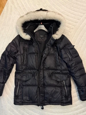 Rockandblue Vinterjacka  - Säljer en svart Rockandblue jacka i storlek L. Jackan är i jättefint skick, endast använd max 3 gånger.  Den är varm och stilren med päls på huvan och snygga detaljer. Det enda som finns att anmärka på är ett litet hål längst ut på ena ärmen (se bild). Påverkar inte funktionen.  I övrigt är jackan mycket fräsch och väl omhändertagen.