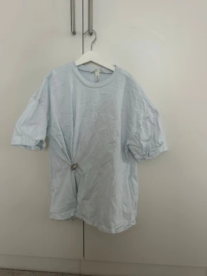 Ljusblå t-shirt från H&M med knut - Säljer en ljusblå t-shirt från H&M i storlek S. T-shirten har en enkel design med rund hals och korta ärmar. Den är gjord i mjuk bomull och har en snygg detalj med knut framtill som ger en chill vibe.