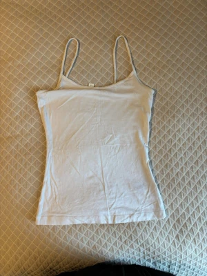 Vit ribbad linnetopp från H&M - Säljer en enkel och stilren vit linnetopp från H&M med tunna axelband och ribbad struktur. Toppen är figurnära och perfekt för varma dagar eller som lager under andra plagg. Klassisk modell som passar till det mesta.