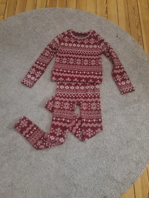 Röda leggings och tröja med vintermönster - Mysig röd pyjamas/underställ med vitt vintermönster av snöflingor, hjärtan och zigzag. Tröjan är i st M/L och byxorna i st S. Peraonligen skulle inte jag säga att tröjan är jätte stor i stolek. Hör gjärna av er om ni bara är intresserade i en del. Tillverkade i stretchigt material (98% polyester, 2% elastan) som är superbekvämt. Perfekta för julmys eller chill hemma. Midjan är normal och passformen är tight. 