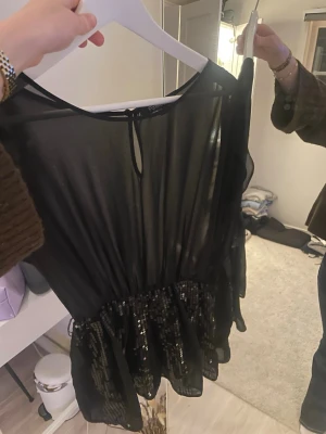 Svart kort klänning med paljetter - Säljer en svart kort klänning från Forever 21 med transparent överdel och glittrig paljettkjol. Klänningen har rund hals och är ärmlös. Den är k mycket gott skick och inga defekter. Hör av er för fler frågor💗💗