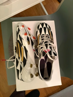 Adidas fotbollsskor svart/vit/guld - Säljer ett par riktigt snygga Adidas fotbollsskor med svartvitt grafiskt mönster och guldiga detaljer på sidorna. Skorna har snörning, platt sula med dobbar och är tillverkade i syntetmaterial. Perfekta för dig som vill sticka ut på planen! Unikt par, limited edition adidas adizero f50. I väldigt bra skick! Låda nedkommer! Storlek 44! Kan skicka flera bilder vid intresse😁
