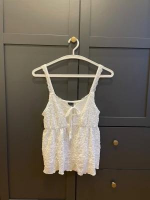 Vitt spetsigt linne från Gina - Supersöt vit linnetopp med spetsiga axelband och knyt framtill. Linnet är lite längre baktill, är från Gina Tricot i storlek S. Pris kan diskuteras, skriv privat vid intresse! 
