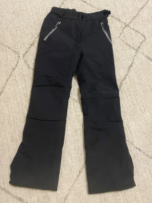 Svarta täckbyxor från Everest - Svarta täckbyxor från Everest med två dragkedjeförsedda fickor fram och justerbar midja. Byxorna har en rak passform och är gjorda i slitstarkt syntetmaterial, perfekta för kalla dagar. Reflekterande detalj på baksidan av benet för extra synlighet. Använd få gånger köptes för 600💕 kom med pris förslag!!!!😊😊😊😊😊