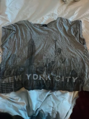 Grå t-shirt med New York City-tryck - Säljer en grå t-shirt från Mango med coolt New York City-tryck framtill, inklusive Frihetsgudinnan och skyskrapor. T-shirten har korta ärmar och en avslappnad passform. Den är mycket mjuk. Hör av er vid fler frågor💗