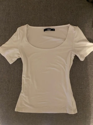 Vit topp med rund hals från Bik Bok - Säljer en vit topp från Bik Bok i storlek XS. Toppen har en rundad, djup halsringning och korta ärmar. Materialet är mjukt och stretchigt, perfekt för en enkel och clean look. Passformen är normal och toppen är enfärgad utan mönster.