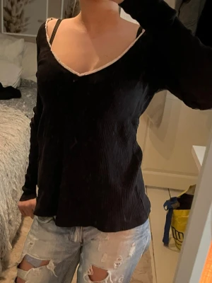 Odd molly topp - Intressekoll på min favorit topp Svart långärmad topp från Odd Molly med ribbad struktur och v-ringad hals. Dekorerad med vit spetskant och liten rosett framtill. Modellen är figurnära och har en mjuk bomullskänsla, perfekt för dig som gillar stilrena detaljer🫶🏼