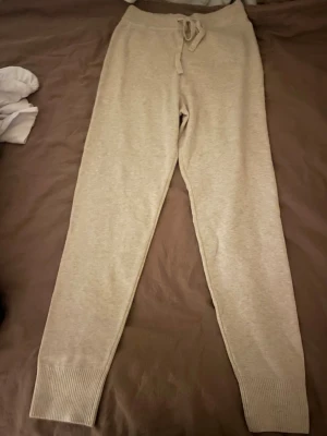 Beige mjukisbyxor från H&M med snörning - Säljer ett par beige mjukisbyxor från H&M i storlek S. Byxorna har ribbade muddar vid bensluten och snörning i midjan för extra komfort. Materialet är mjukt och passar perfekt för chill dagar. Enkla att matcha med hoodies eller t-shirts.