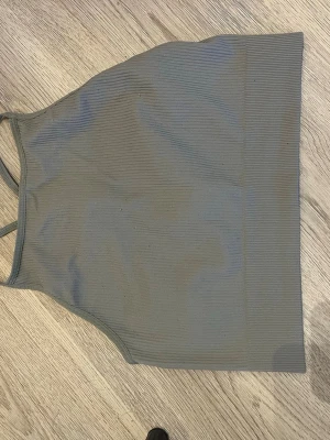 Olivgrön croppad linne - Snygg olivgrön croppad linne med smala axelband och ribbad struktur. Toppen har en sportig look med rundad hals och ärmlös design, perfekt för att matcha med jeans eller shorts. Materialet är mjukt och stretchigt för en bekväm passform.