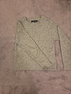 Grön stickad tröja från Vero Moda - Mysig grönmelerad stickad tröja från Vero Moda i storlek XS. Tröjan har rund halsringning, långa ärmar och ribbade muddar vid ärmslut och nederkant. Perfekt för kyliga dagar och enkel att matcha med jeans eller kjol.