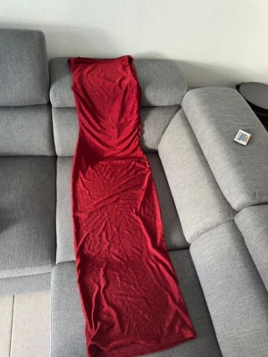 Röd långklänning med glitter - Säljer en snygg röd långklänning med glittrigt tyg och ärmlös design. Klänningen har en figurnära passform och rund halsringning. Perfekt för dig som vill sticka ut med en elegant och modern look. Materialet känns mjukt och följsamt mot kroppen.