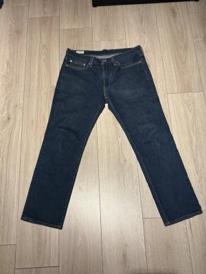 Levi's 514 mörkblå jeans W32 L30 - Säljer ett par Levi's 514 jeans i mörkblå denim med klassisk femficksdesign och kontrastsömmar. Modellen har rak passform och normal midja. Materialet är slitstarkt bomullsjeans och bakfickorna har den ikoniska Levi's-labeln. Perfekt för dig som gillar tidlös stil.