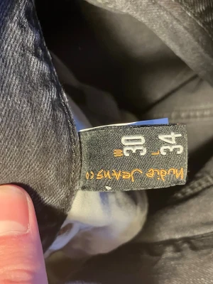 Svarta jeans från Nudie Jeans Co - Säljer ett par svarta jeans från Nudie Jeans straight/regular fit. Storleken är w30 L34. Har använt de cirka 10 gånger och tvättat de cirka 2 gånger. Hör av dig vid frågor eller funderingar!