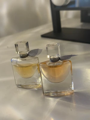 2 st Lancome mini parfymer 4ml - Två små flaskor Lancôme parfym, båda med dekorativ rosett vid halsen. Varje flaska innehåller 4 ml vardera (0.13 fl.oz) Eau de Parfum. Perfekt storlek för väskan eller resan. Den ena är lite mer använd, säljes tsm för 150kr.