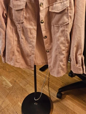 Rosa manchester overshirt från SHEIN - Säljer en rosa overshirt från SHEIN i mjuk manchester med klassisk krage och stora bröstfickor. Jackan har knappar framtill och långa ärmar med knapp vid mudden. Perfekt för lager-på-lager och chill stil.