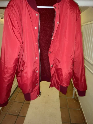 Röd teddy bomberjacka IN&UT med dragkedja på båda sidor får två olika unika stilar - Säljer en röd bomberjacka som man kan vända ut och in för en helt ny look. med teddyfoder och ribbade muddar. Jackan har dragkedja och tryckknappar framtill samt två fickor. Utsidan är slät och insidan är fluffig teddy, 