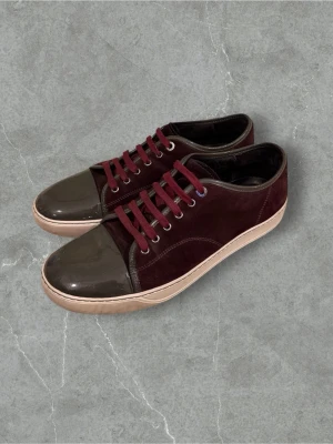 Lanvins  - Snygga sneakers i vinröd mocka med mörkgrå lackad tå och matchande detaljer. Skorna har vinröda snören, beige sula och rund tå. Perfekt för dig som vill ha en unik och stilren look till vardags. Materialmixen ger en lyxig känsla och färgkombon sticker ut.