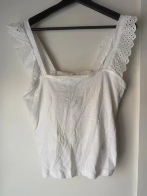 Ny Vit broderad linnetopp från H&M - Säljer en söt vit linnetopp från H&M i storlek M. Toppen har breda axelband med broderade spetsdetaljer och en rak, enkel passform. Perfekt till sommaren och lätt att matcha med jeans eller kjol.